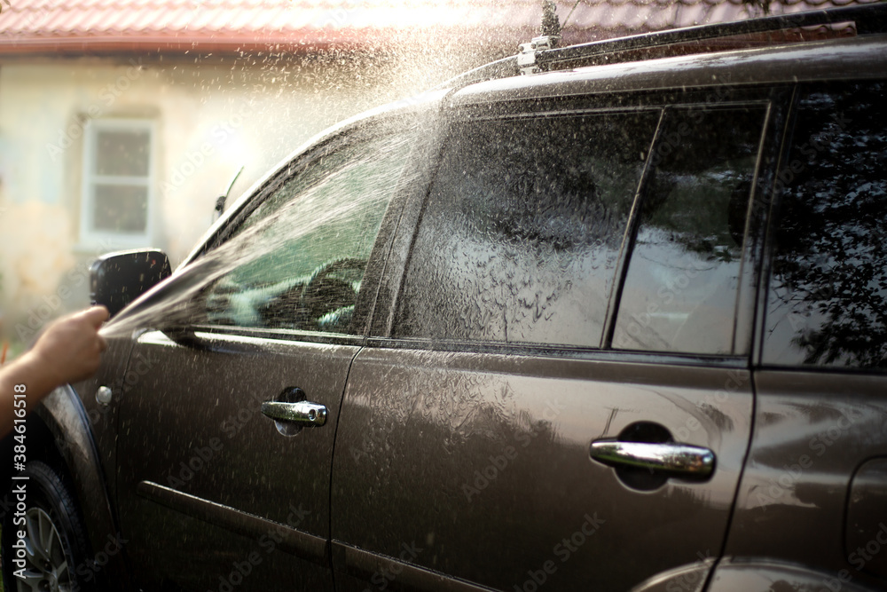 a man with a hose washes the car in the courtyard of the house, a stream of water is sprayed on the glass.