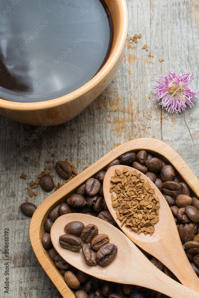 Black coffee in a cup and coffee beans in a wooden spoon on a wooden table. Black coffee in a cup and coffee beans in a wooden spoon on a wooden table.