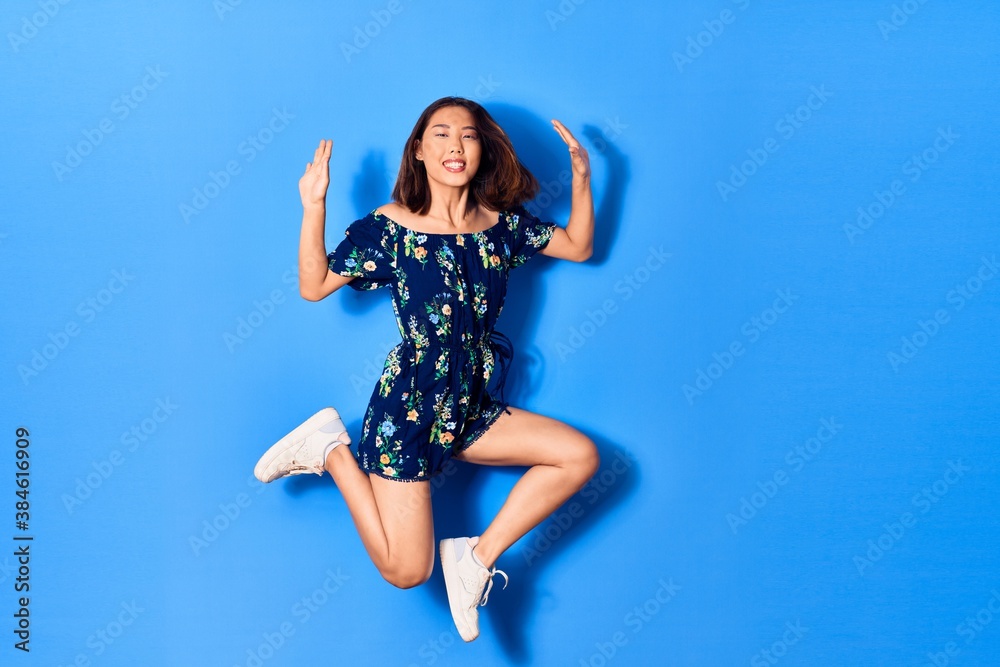 Naklejka premium Young beautiful chinese woman wearing casual clothes smiling happy. Jumping with smile on face over isolated blue background
