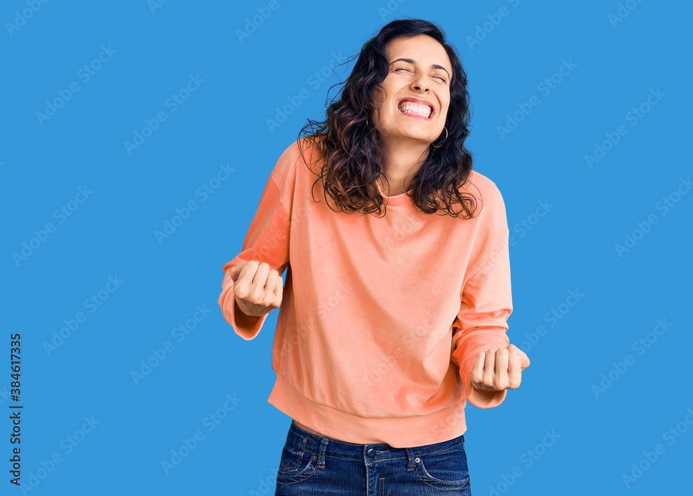 Young beautiful hispanic woman wearing casual clothes very happy and excited doing winner gesture with arms raised, smiling and screaming for success. celebration concept. Young beautiful hispanic woman wearing casual clothes very happy and excited doing winner gesture with arms raised, smiling and screaming for success. celebration concept.