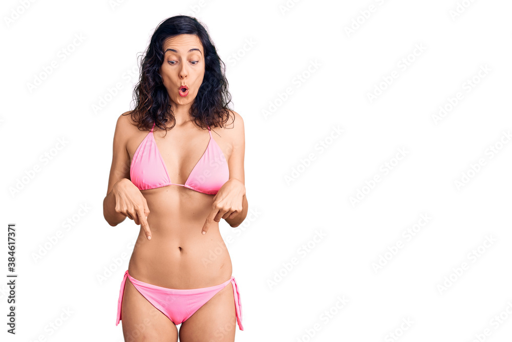 Young beautiful hispanic woman wearing bikini pointing down with fingers showing advertisement, surprised face and open mouth Young beautiful hispanic woman wearing bikini pointing down with fingers showing advertisement, surprised face and open mouth