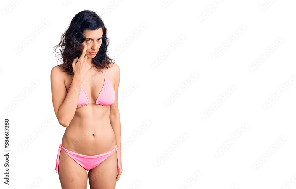 Young beautiful hispanic woman wearing bikini pointing to the eye watching you gesture, suspicious expression