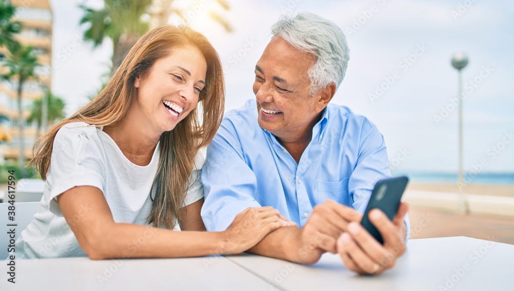 Middle age couple in love sitting at the terrace of coffee shop using smartphone happy and cheerful together Middle age couple in love sitting at the terrace of coffee shop using smartphone happy and cheerful together