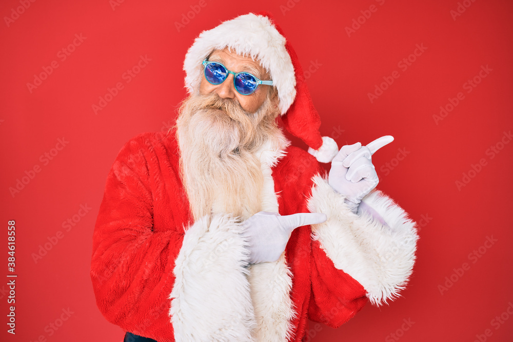 Old senior man wearing santa claus costume and sunglasses smiling and looking at the camera pointing with two hands and fingers to the side. Old senior man wearing santa claus costume and sunglasses smiling and looking at the camera pointing with two hands and fingers to the side.