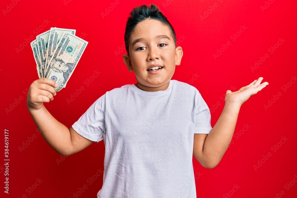 Little boy hispanic kid holding 20 dollars banknotes celebrating achievement with happy smile and winner expression with raised hand Little boy hispanic kid holding 20 dollars banknotes celebrating achievement with happy smile and winner expression with raised hand