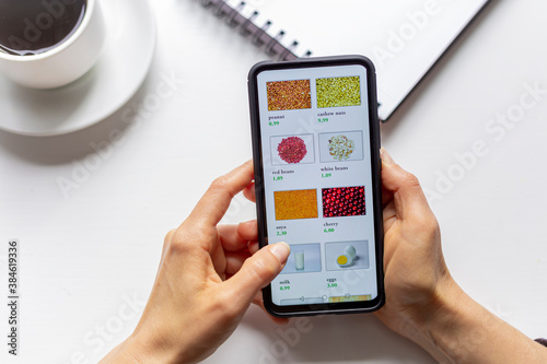 Woman using smartphone buys food online in the internet shop store. Woman's hand on the mobile phone screen selects the goods remotely at home .