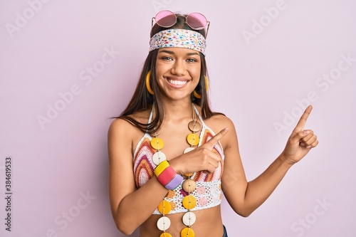 Beautiful hispanic woman wearing bohemian and hippie style smiling and looking at the camera pointing with two hands and fingers to the side.