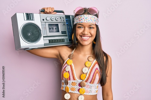 Beautiful hispanic woman wearing hippie style holding boom box looking positive and happy standing and smiling with a confident smile showing teeth