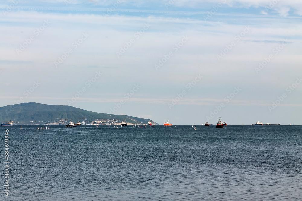 Small sailing yachts and ships queuing up for unloading at the seaport at the exit from the sea bay.