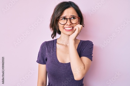 Young beautiful woman wearing casual clothes and glasses looking stressed and nervous with hands on mouth biting nails. anxiety problem.