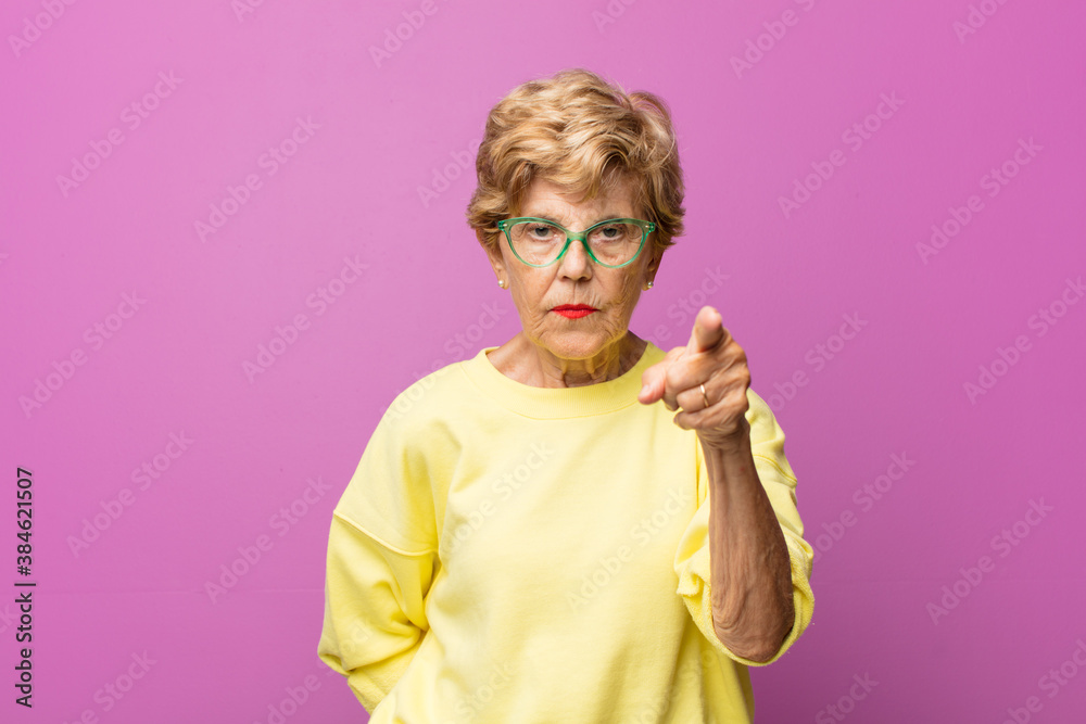 old pretty woman pointing at camera with an angry aggressive expression ...