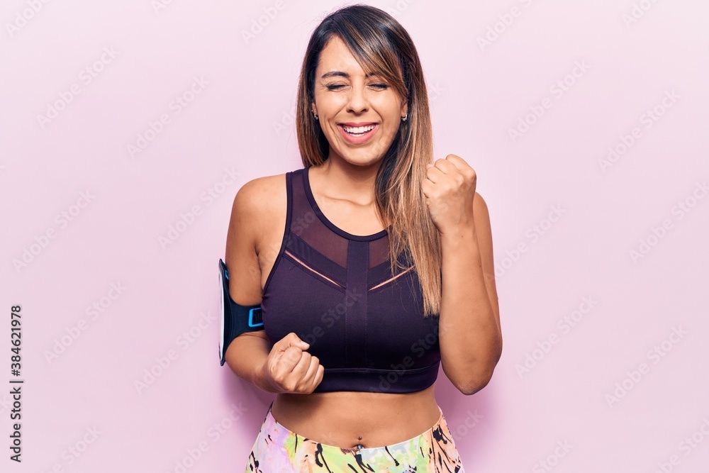 Young beautiful woman wearing sportswear with smartphone on arm celebrating surprised and amazed for success with arms raised and eyes closed