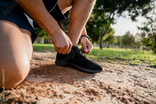 Young male athlete bending down tying running shoes before exercising on outdoor running path