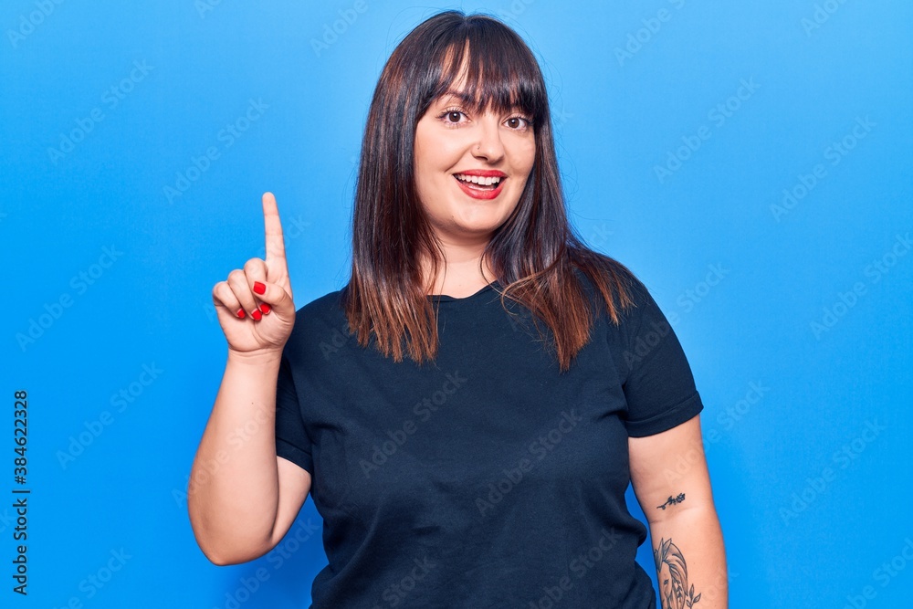 Young plus size woman wearing casual clothes smiling with an idea or question pointing finger up with happy face, number one Young plus size woman wearing casual clothes smiling with an idea or question pointing finger up with happy face, number one