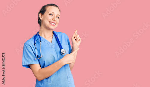 Young beautiful blonde woman wearing doctor uniform and stethoscope smiling and looking at the camera pointing with two hands and fingers to the side. photo