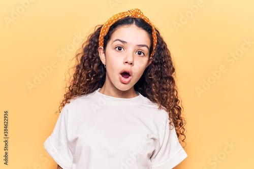 Beautiful kid girl with curly hair wearing casual clothes scared and amazed with open mouth for surprise, disbelief face
