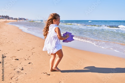 Adorable blonde child on back view wearing summer dress. Holding beach bucket at the sand
