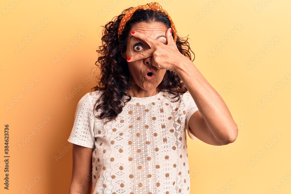 Middle age beautiful woman wearing casual t shirt peeking in shock covering face and eyes with hand, looking through fingers afraid Middle age beautiful woman wearing casual t shirt peeking in shock covering face and eyes with hand, looking through fingers afraid