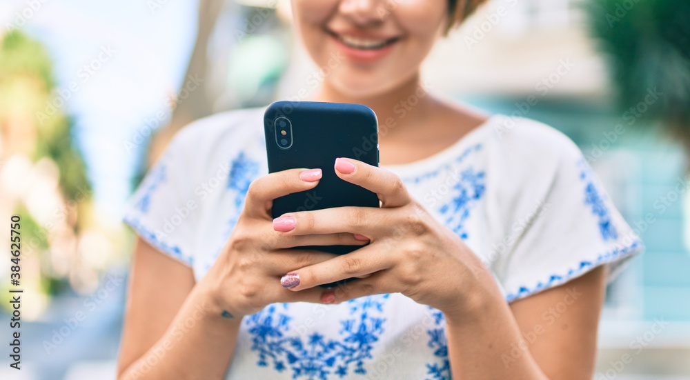 Fototapeta premium Young latin tourist girl on vacation smiling happy using smartphone at the city.