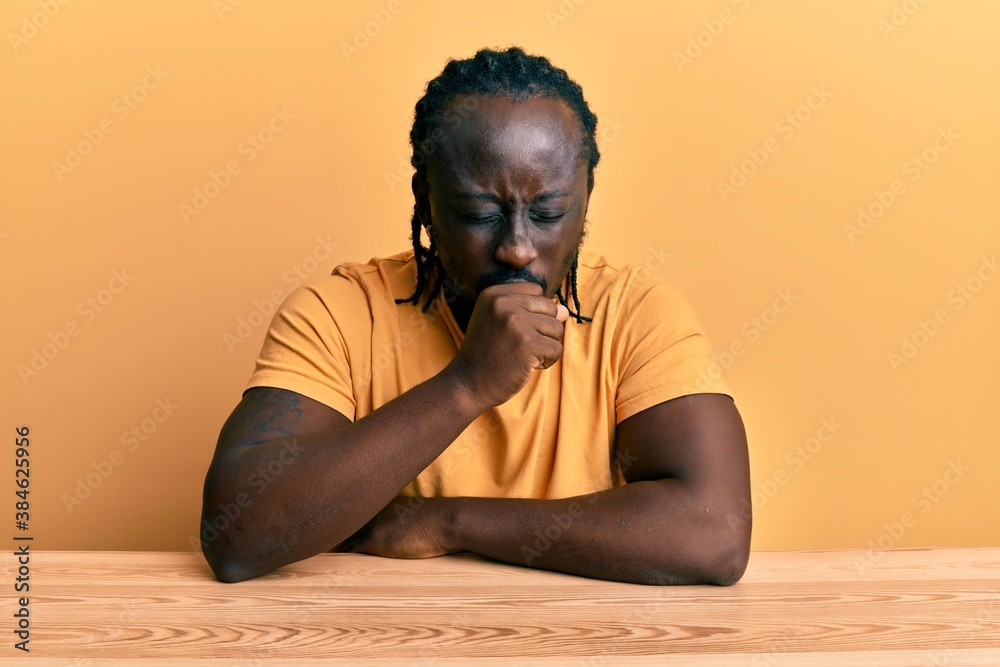 Handsome young black man wearing casual clothes sitting on the table feeling unwell and coughing as symptom for cold or bronchitis. health care concept. Handsome young black man wearing casual clothes sitting on the table feeling unwell and coughing as symptom for cold or bronchitis. health care concept.