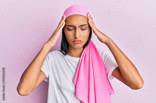 Young brunette woman wearing breast cancer support pink scarf suffering from headache desperate and stressed because pain and migraine. hands on head. © Krakenimages.com