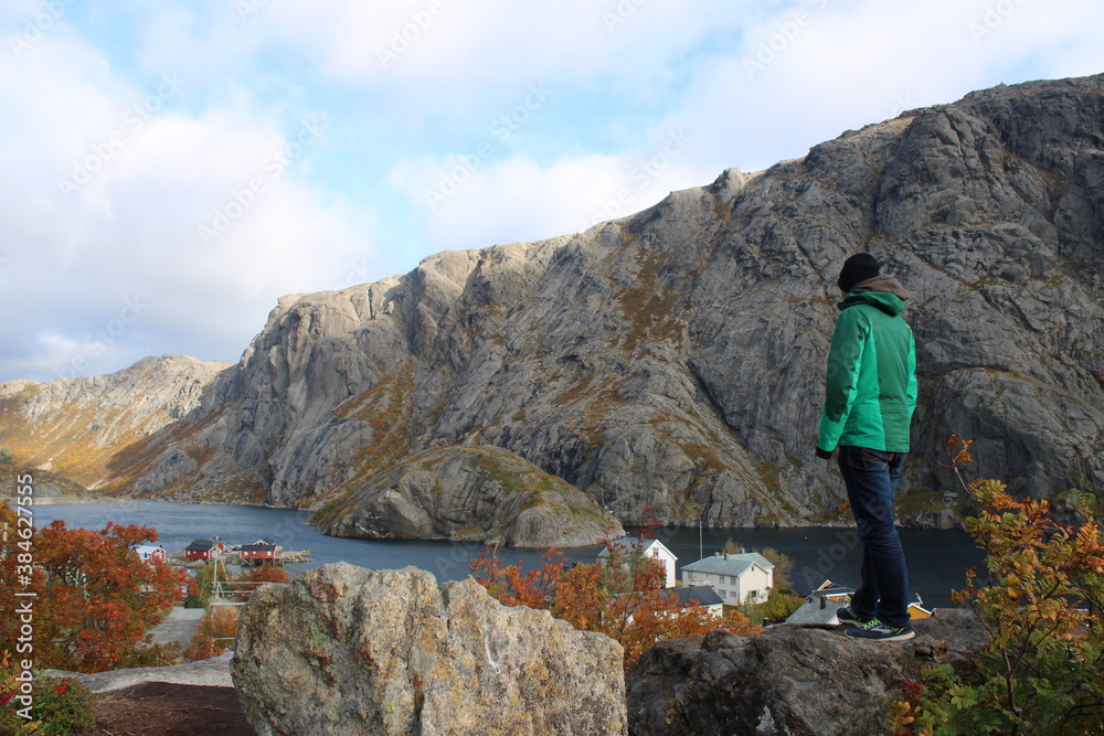 Man standing on a rock and enjoying a beautiful view on Nusfjord village on Lofoten islands in autumn. 