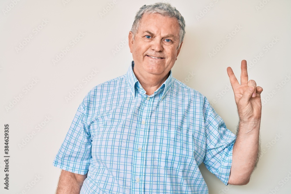 Senior grey-haired man wearing casual clothes smiling with happy face winking at the camera doing victory sign. number two. Senior grey-haired man wearing casual clothes smiling with happy face winking at the camera doing victory sign. number two.