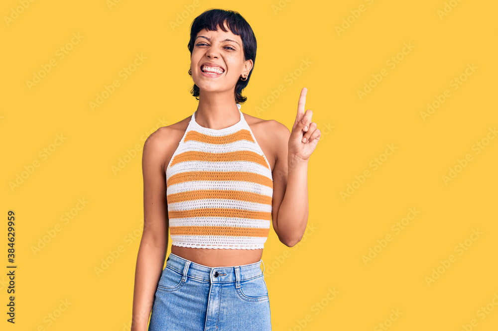 Young brunette woman with short hair wearing casual clothes showing and pointing up with finger number one while smiling confident and happy. Young brunette woman with short hair wearing casual clothes showing and pointing up with finger number one while smiling confident and happy.