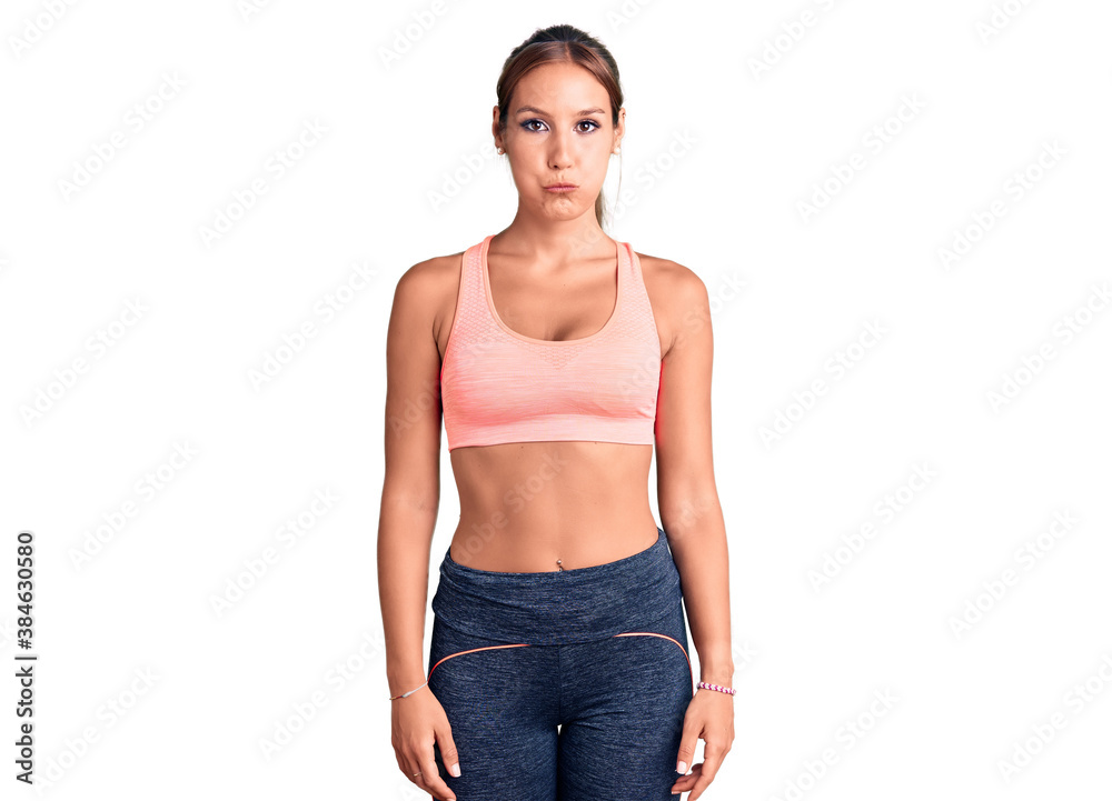 Young beautiful hispanic woman wearing sportswear puffing cheeks with funny face. mouth inflated with air, crazy expression. Young beautiful hispanic woman wearing sportswear puffing cheeks with funny face. mouth inflated with air, crazy expression.