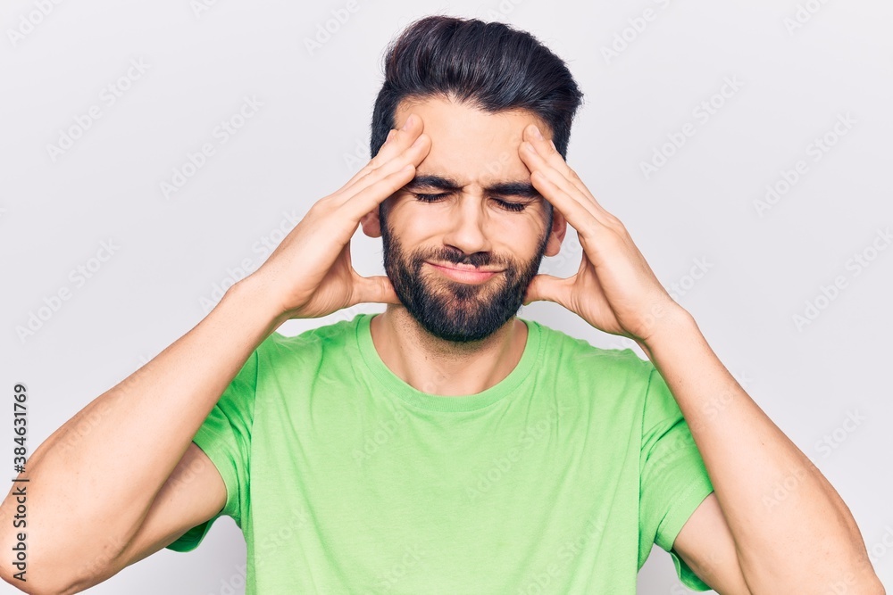 Young handsome man with beard wearing casual t-shirt suffering from headache desperate and stressed because pain and migraine. hands on head. Young handsome man with beard wearing casual t-shirt suffering from headache desperate and stressed because pain and migraine. hands on head.