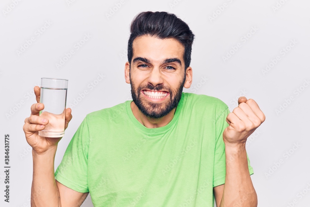 Young handsome man with beard drinking glass of water screaming proud, celebrating victory and success very excited with raised arm Young handsome man with beard drinking glass of water screaming proud, celebrating victory and success very excited with raised arm