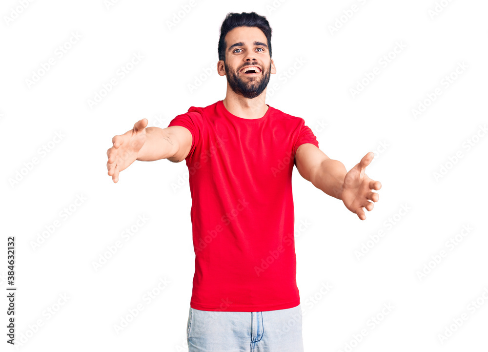 Young handsome man with beard wearing casual t-shirt looking at the camera smiling with open arms for hug. cheerful expression embracing happiness.