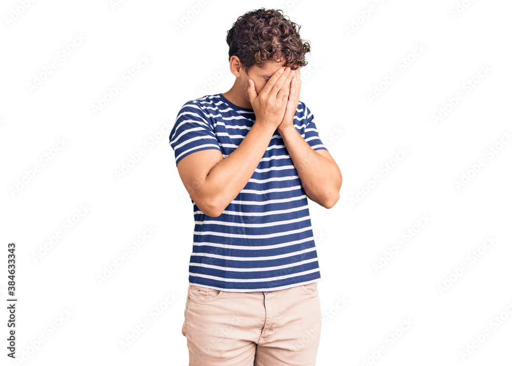 Young handsome man with curly hair wearing casual clothes with sad expression covering face with hands while crying. depression concept. Young handsome man with curly hair wearing casual clothes with sad expression covering face with hands while crying. depression concept.