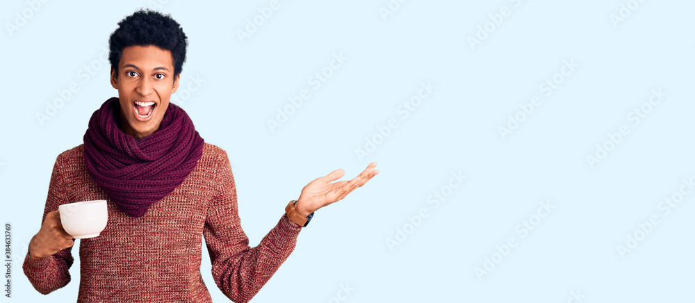Young african american man wearing winter scarf and drinking a cup of hot coffee celebrating victory with happy smile and winner expression with raised hands Young african american man wearing winter scarf and drinking a cup of hot coffee celebrating victory with happy smile and winner expression with raised hands