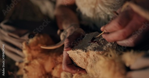 Primitive hunter writing or drawing in blood on a stone by the light of a campfire at noght in a close up on his hands. Creating first cave art with petroglyphs. photo