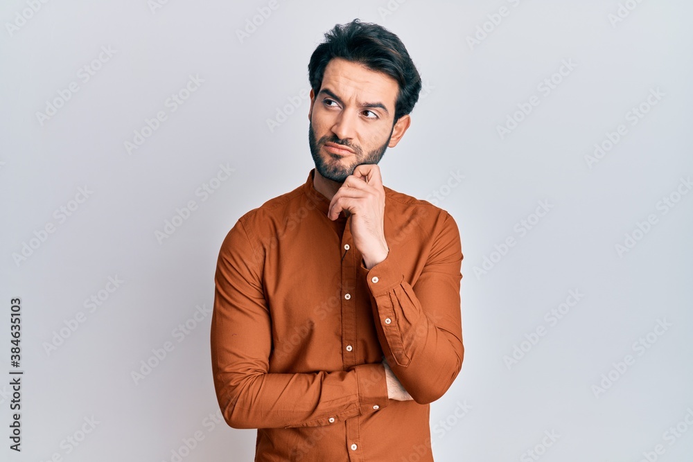 Young hispanic man wearing casual clothes thinking concentrated about doubt with finger on chin and looking up wondering Young hispanic man wearing casual clothes thinking concentrated about doubt with finger on chin and looking up wondering