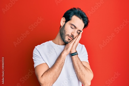 Young hispanic man wearing casual white tshirt sleeping tired dreaming and posing with hands together while smiling with closed eyes.