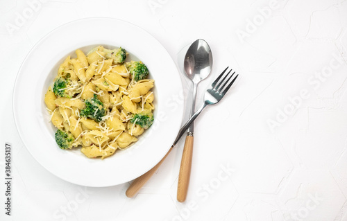 Pasta with green vegetables, broccoli, melted cheese and creamy sauce in white bowl on white table.