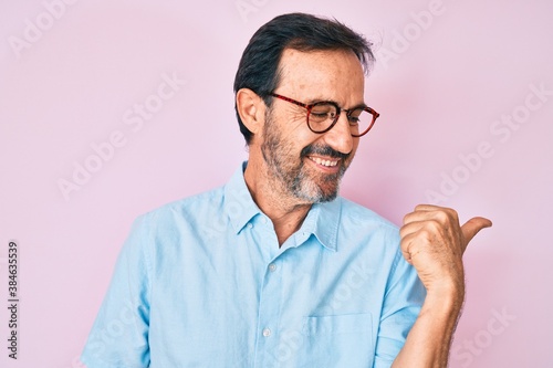 Middle age hispanic man wearing casual clothes and glasses pointing thumb up to the side smiling happy with open mouth