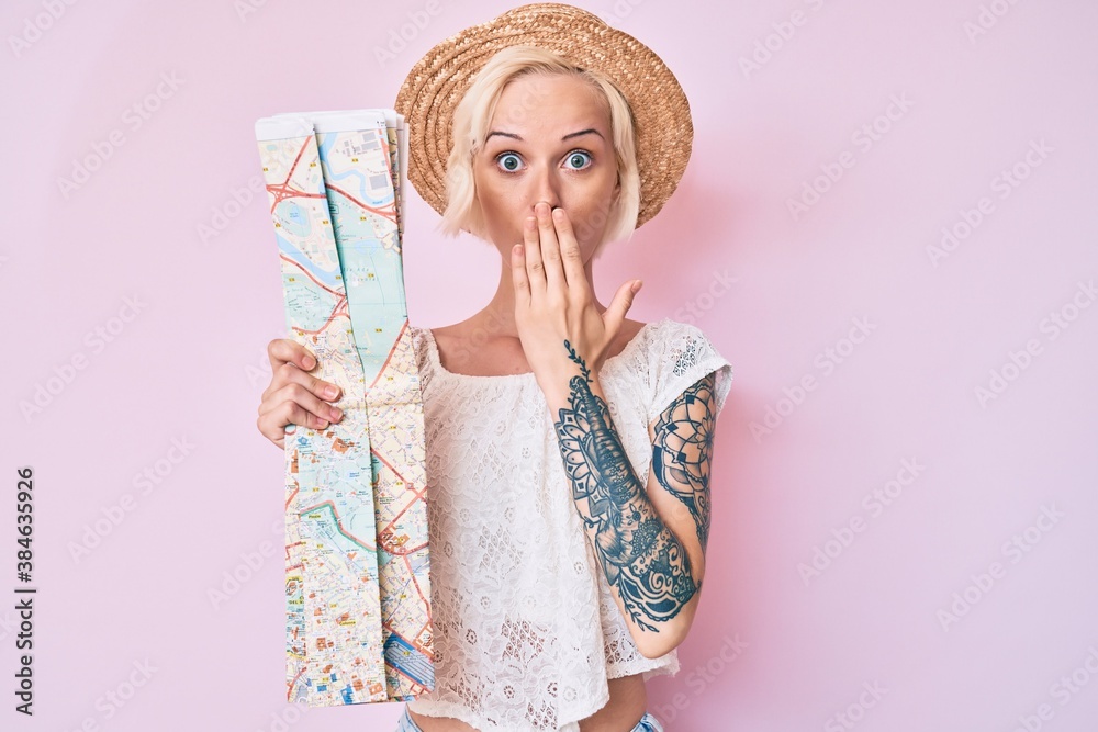 Young blonde woman wearing summer hat holding city map covering mouth with hand, shocked and afraid for mistake. surprised expression Young blonde woman wearing summer hat holding city map covering mouth with hand, shocked and afraid for mistake. surprised expression