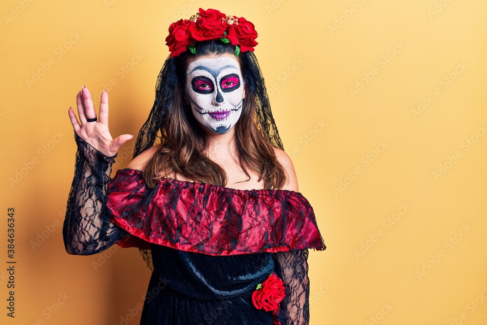 Φωτογραφία Young woman wearing day of the dead costume over yellow showing and pointing up with fingers number five while smiling confident and happy
