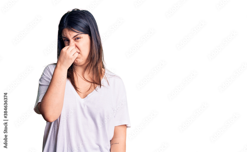 Young beautiful brunette woman wearing casual t-shirt smelling something stinky and disgusting, intolerable smell, holding breath with fingers on nose. bad smell Young beautiful brunette woman wearing casual t-shirt smelling something stinky and disgusting, intolerable smell, holding breath with fingers on nose. bad smell