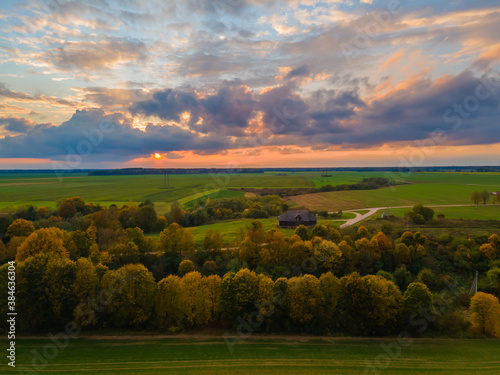 Aerial view of sunset and autumn colors trees in the fields with a house
