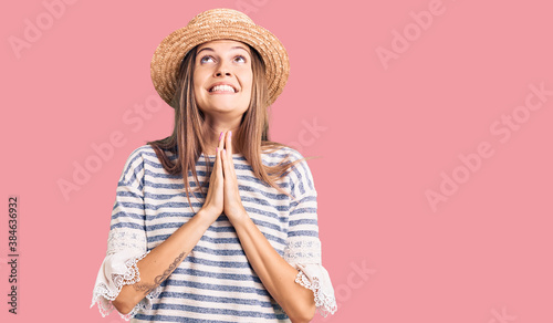 Beautiful caucasian woman wearing summer hat begging and praying with hands together with hope expression on face very emotional and worried. begging.