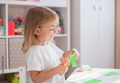 Child with scissors cut paper in play room. Scissor skills activity.