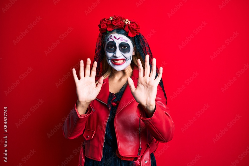 Woman wearing day of the dead costume over red afraid and terrified with fear expression stop gesture with hands, shouting in shock. panic concept. Woman wearing day of the dead costume over red afraid and terrified with fear expression stop gesture with hands, shouting in shock. panic concept.