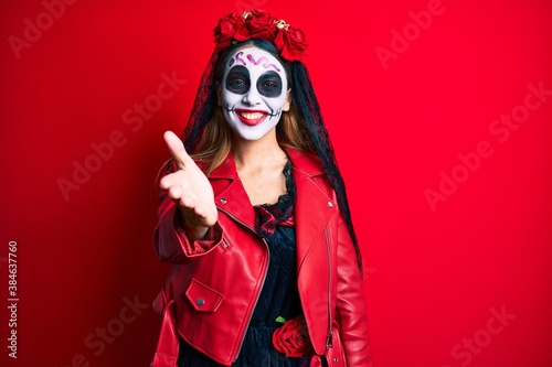 Woman wearing day of the dead costume over red smiling friendly offering handshake as greeting and welcoming. successful business.