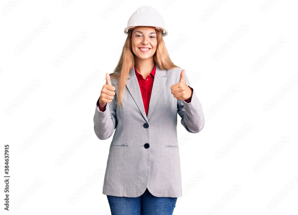 Beautiful young woman wearing architect hardhat success sign doing positive gesture with hand, thumbs up smiling and happy. cheerful expression and winner gesture.