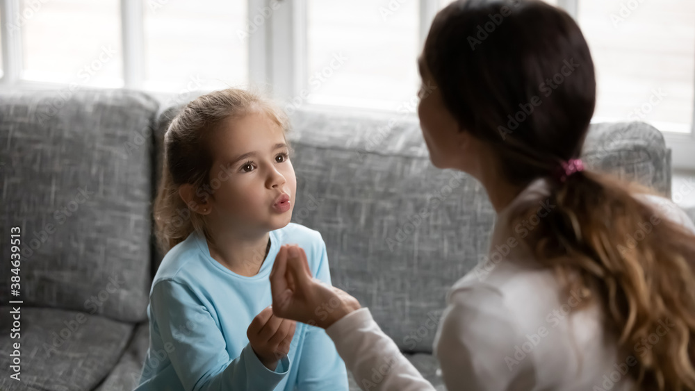 Attentive small Caucasian girl make effort learn pronunciation articulation with female speech therapist or tutor. Little child pronouncing words or sounds with teacher at home. Education concept.