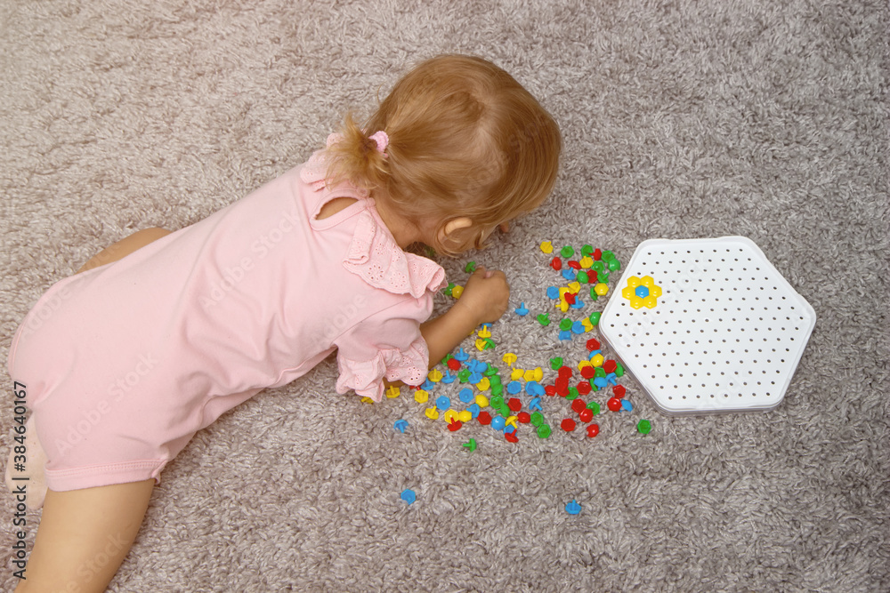 Naklejka premium Board games that develop fine motor skills. The kid girl collects a constructor puzzle from multi-colored plastic parts, top view